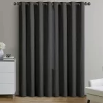 Two flat-pleated linen blackout curtains in a dark gray shade, covering a window with a view of trees and a blue sky