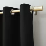 black blackout curtains hanging on a gold curtain rod with silver grommets