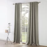 light gray blackout curtains hang on a chrome curtain rod in front of a large window